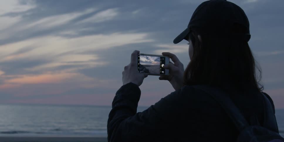 A woman photographs a beach sunset