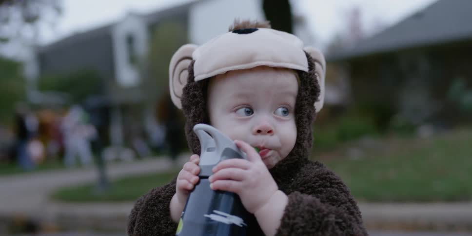 A young child in costume drinks from a bottle