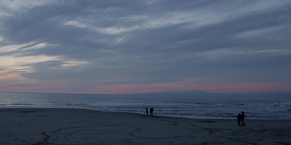 People walk on a beach at sunset