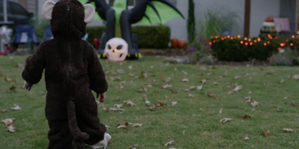A toddler is walking towards a halloween display in front of a house at dusk