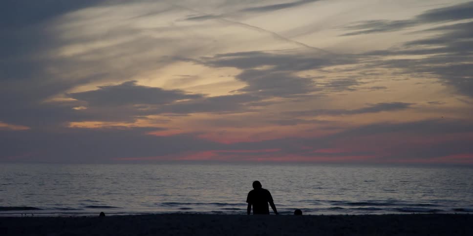 A man and child hold hands on a beach at sunset