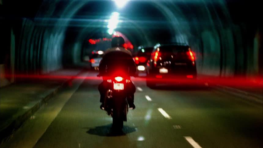 There are multiple cars and a motorcycle driving through a tunnel in the city