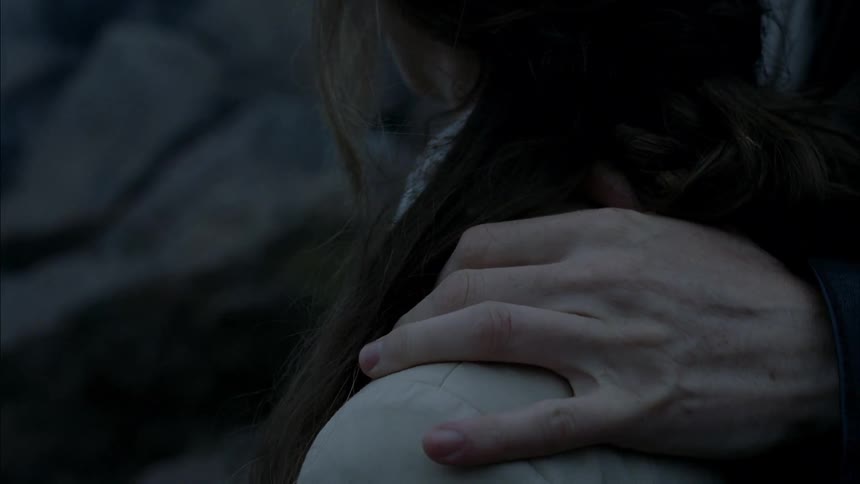 A man's hand is rubbing a woman's shoulder as they stand outside at dusk