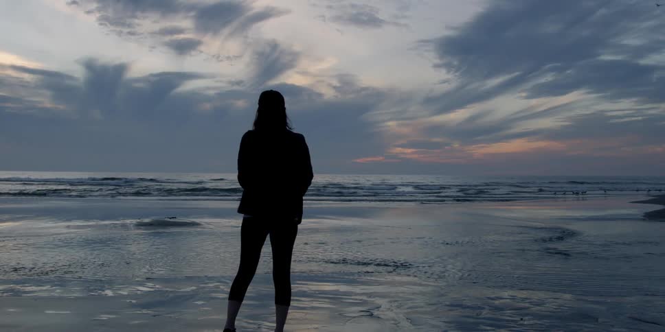 A woman looks out onto the waters from the beach