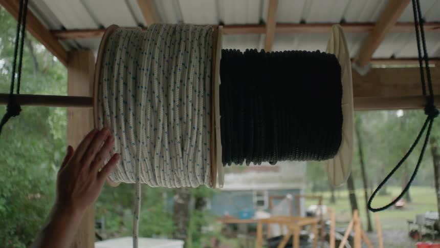 Person unwinding rope from a spool hanging outdoors