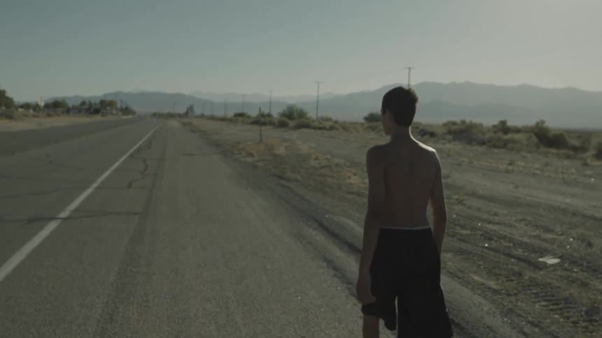 Shirtless man walking down the side of an empty road