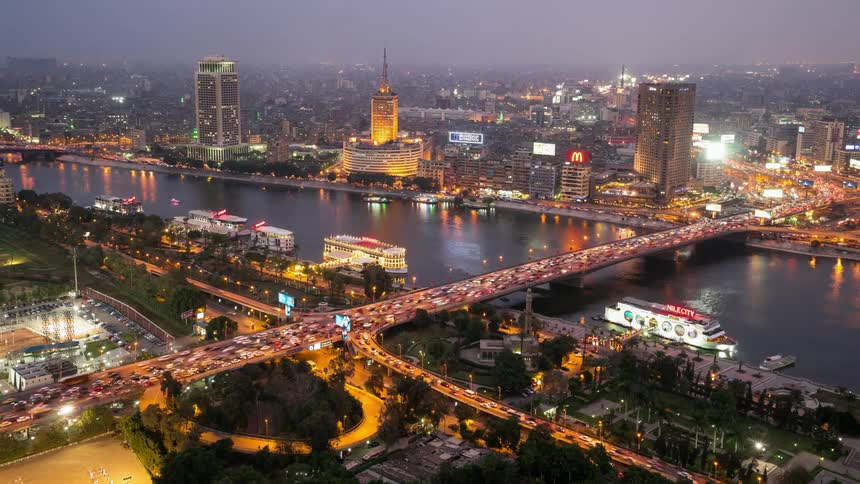 Traffic is flowing over a bridge both ways across a river at dusk