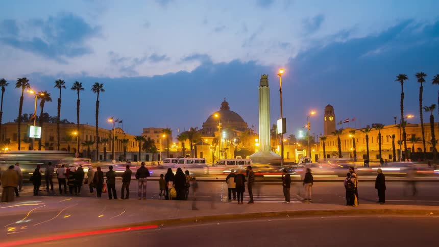 Large group of people waiting at the edge of a city street to cross or get on a bus