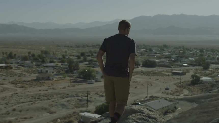 Man climbs onto rocks overlooking a small city