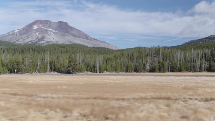 An suv travels on a rural road near trees and mountains