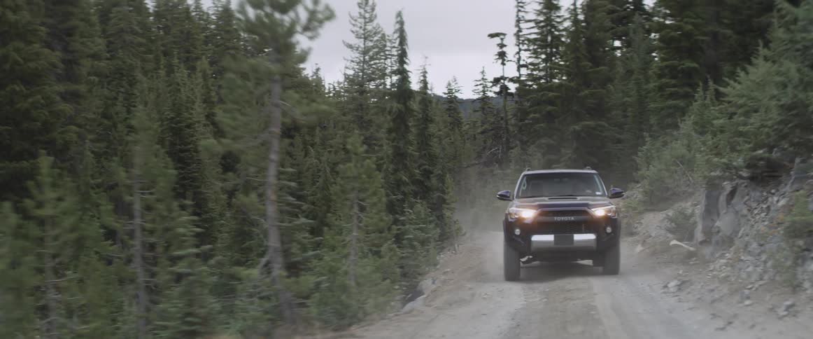 An suv drives up a bumpy dirt road in the forest