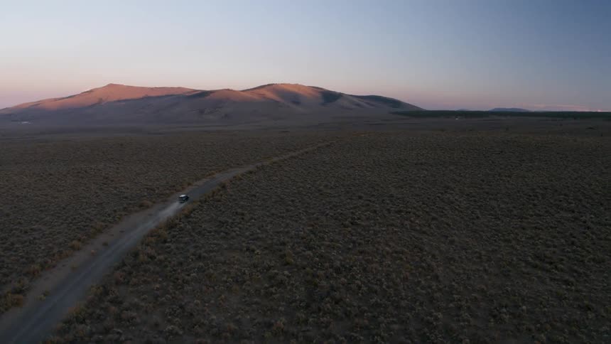 A vehicle travels on a rural dirt road at sunset