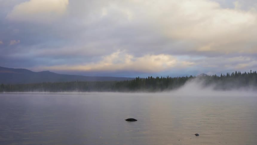Fog rises from a lake on a cloudy day