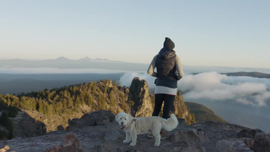 A woman stands atop a mountain with her dog