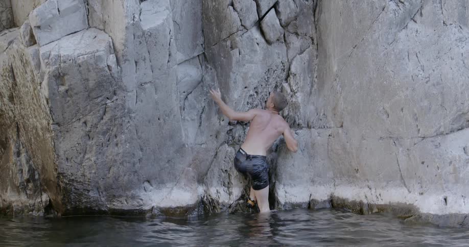 A man pulls himself out of the water by climbing up a rock wall