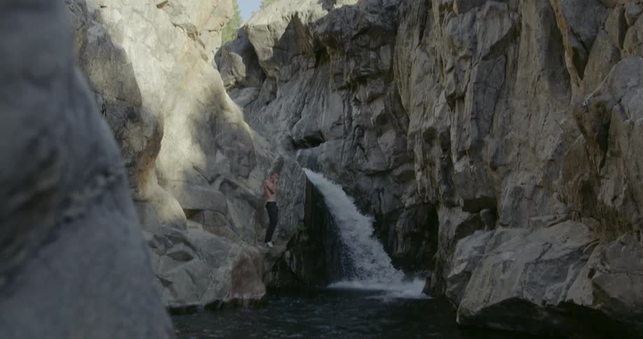 A bare chested man jumps from a cliff into water below