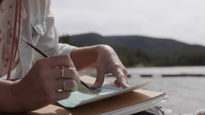 A woman is sitting on a dock painting during the day