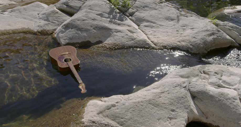 A guitar is floating in a stream between rocks and boulders during the day