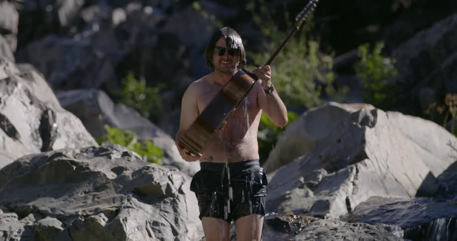 A man dumps water out of a guitar near a stream