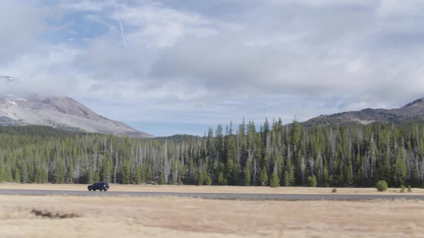 A truck drives down a rural road by a mountain
