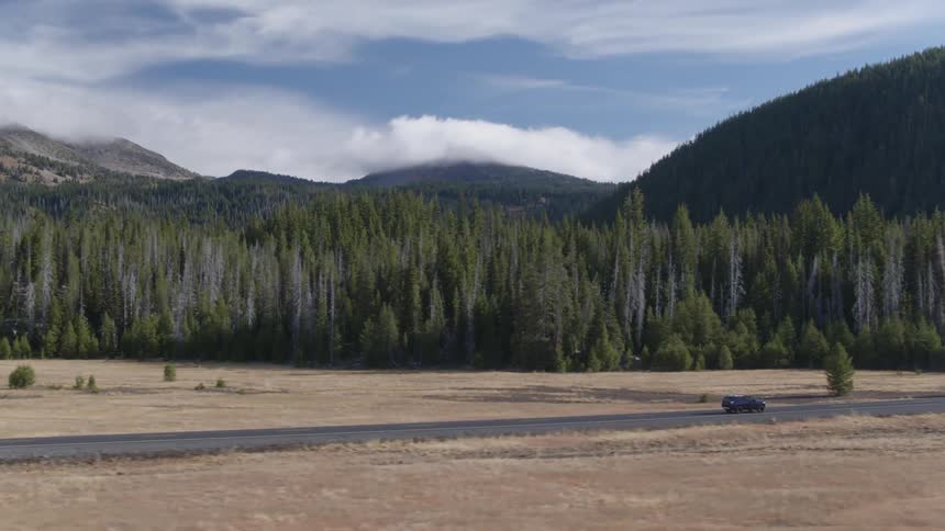 A vehicle drives by forest trees and mountains