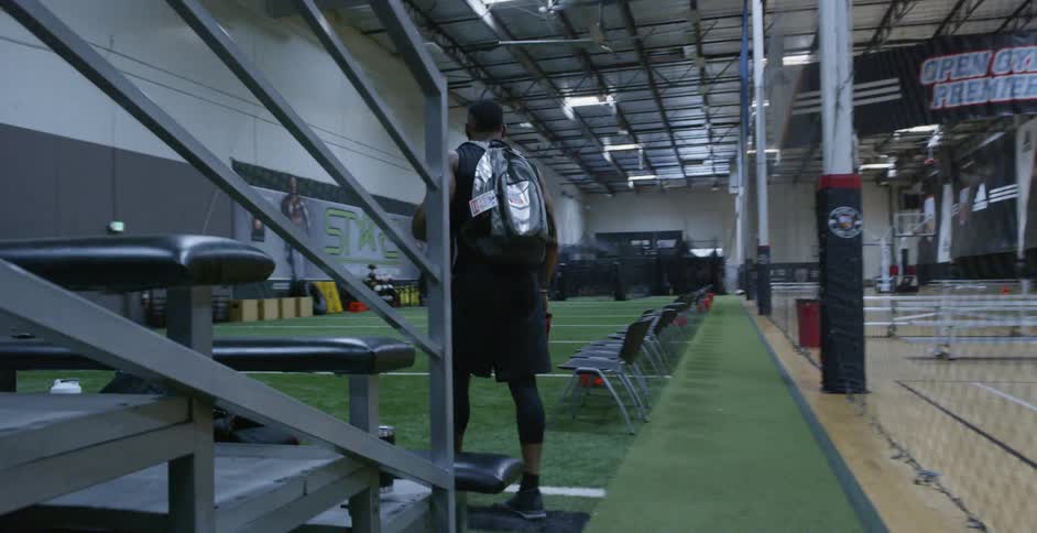 A male athlete carrying his shoes is walking onto an indoor football field