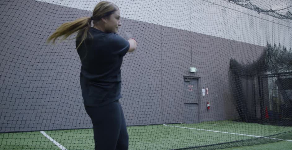 A woman hits softballs indoors