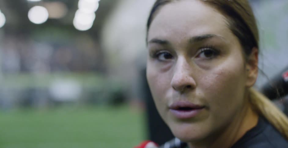 A female athlete is preparing to swing a baseball bat as she trains indoors