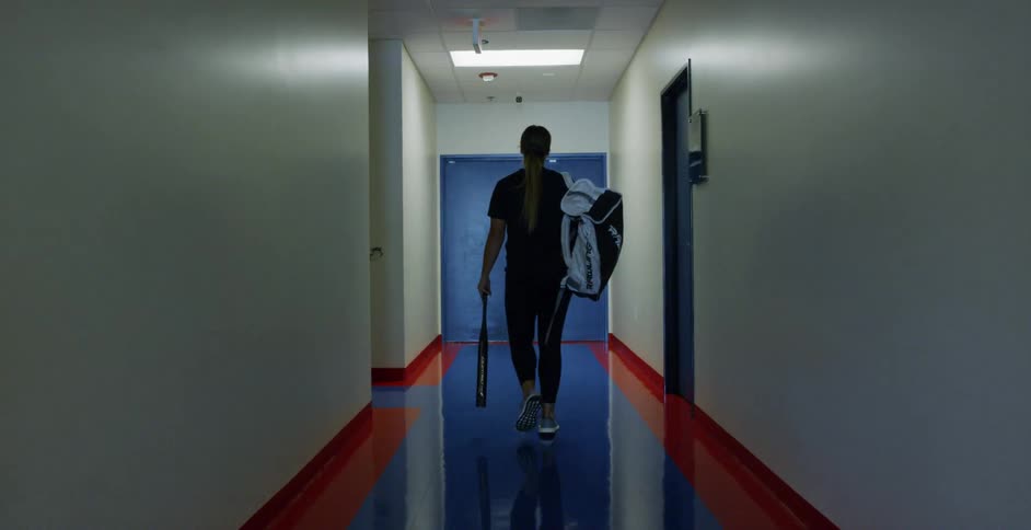 A woman carries softball gear into a training facility