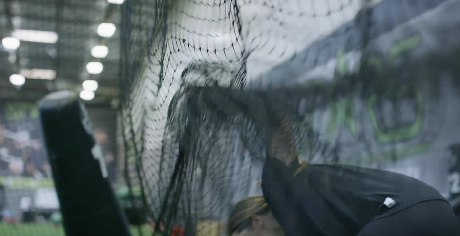 Woman ducks under a net and picks up a baseball bat