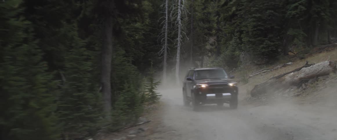 An suv is driving on a dirt road through a forest at dusk