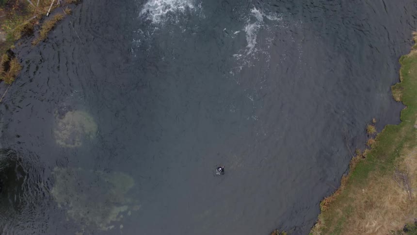 Person fishes in the middle of a stream with a waterfall at the end