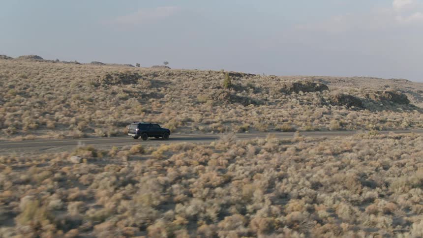 Jeep drives down a country road surrounded by hilly brushy plains