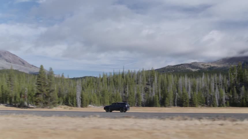 An suv drives down a rural road near forest and mountains