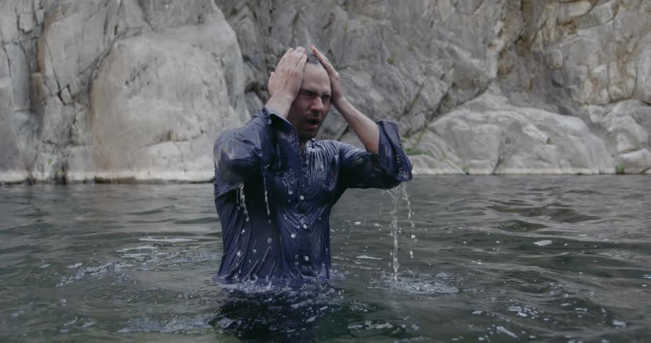 A man emerges from lake water gasping for air fully dressed