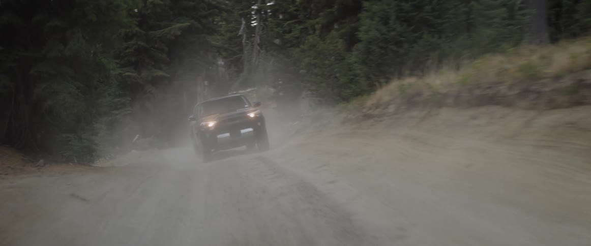 An suv is driving fast on a rural dirt road at dusk