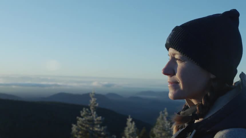 A woman is smiling as she stands looking out at a view on a cold day
