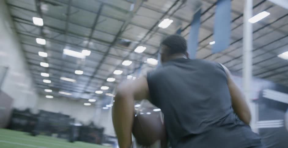 A male athlete is sprinting to catch a football as he trains indoors