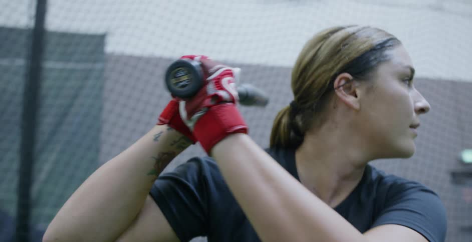A woman hits softballs indoors