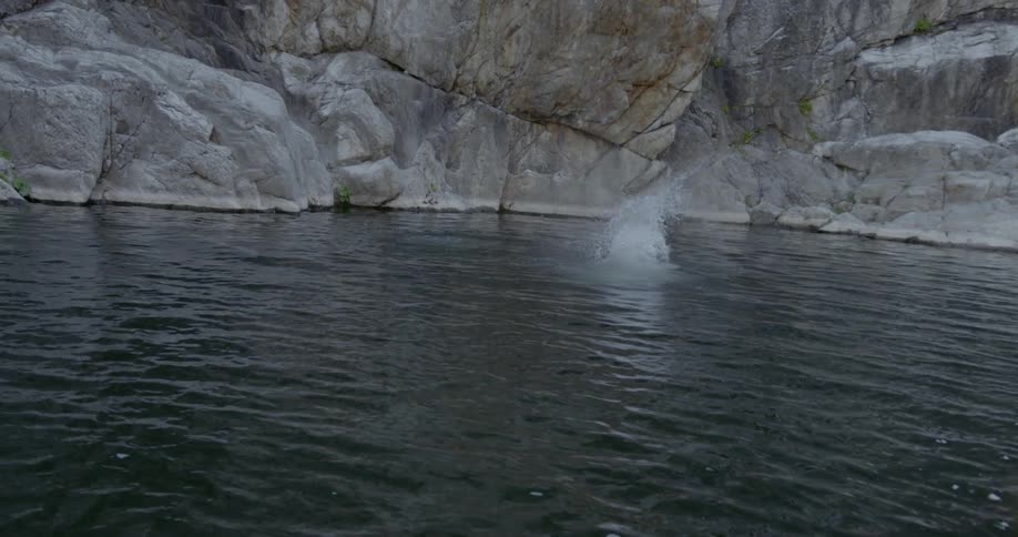 A man jumps backwards off a massive cliff and dives into the water feet first