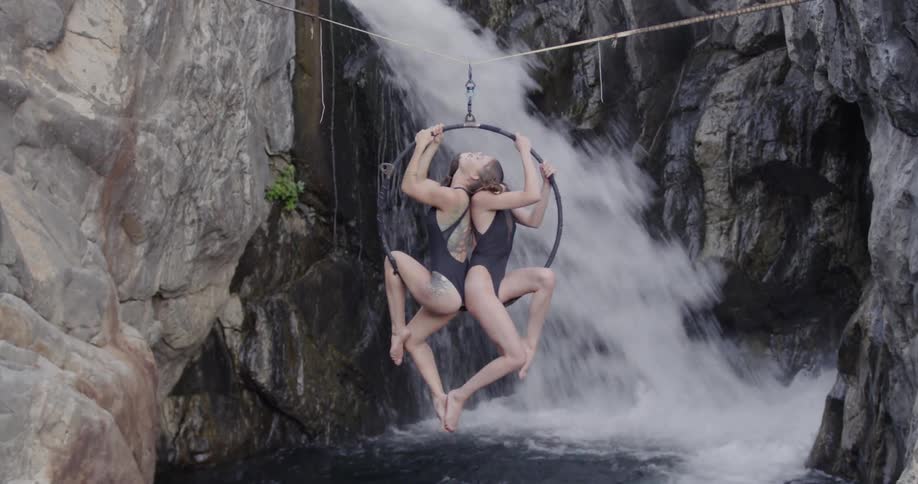 Two beautiful women spin on an aerial hoop hanging in a canyon