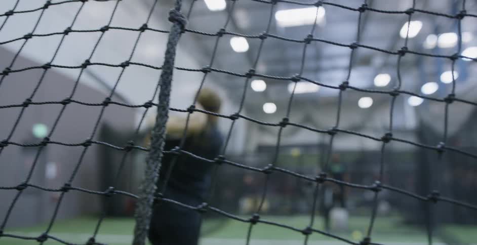 A woman hits softballs indoors