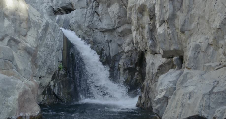 Water flows rapidly down rocks and off waterfall into river