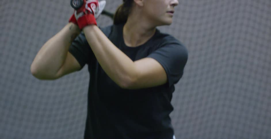 A woman holds a bat in a batting cage