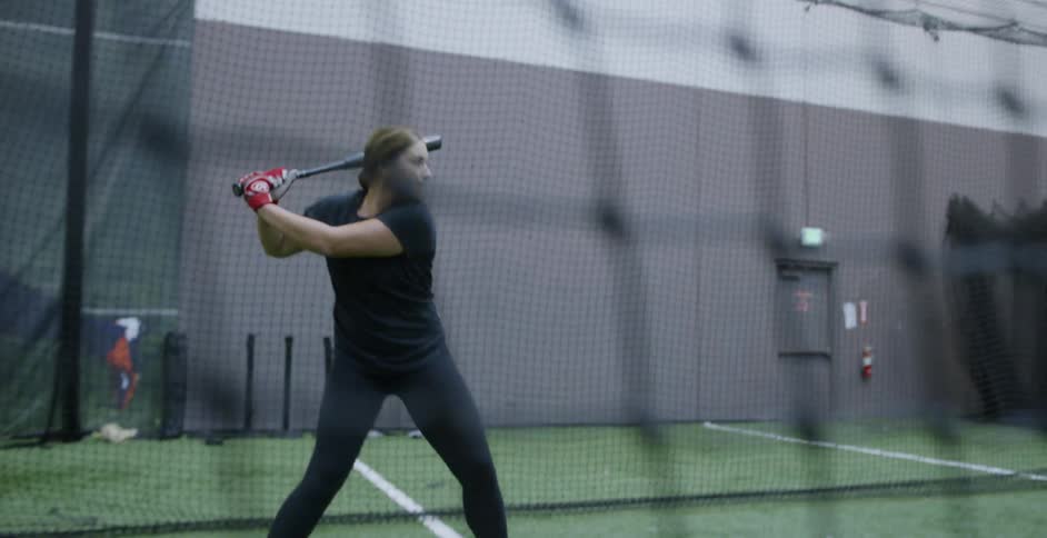 A female athlete is practicing her baseball batting indoors