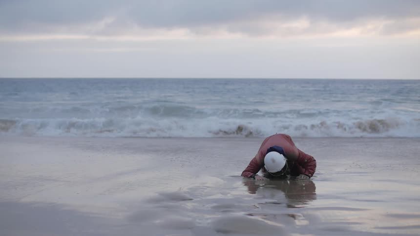 Man wearing helmet slowly gets up from the wet sand