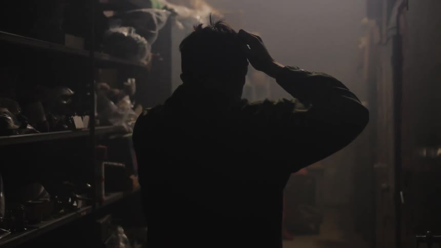 Distraught man walks between filled shelves in a darkened room