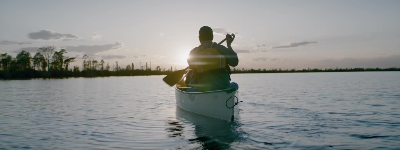 Man rowing a small boat towards a cloudy sunset
