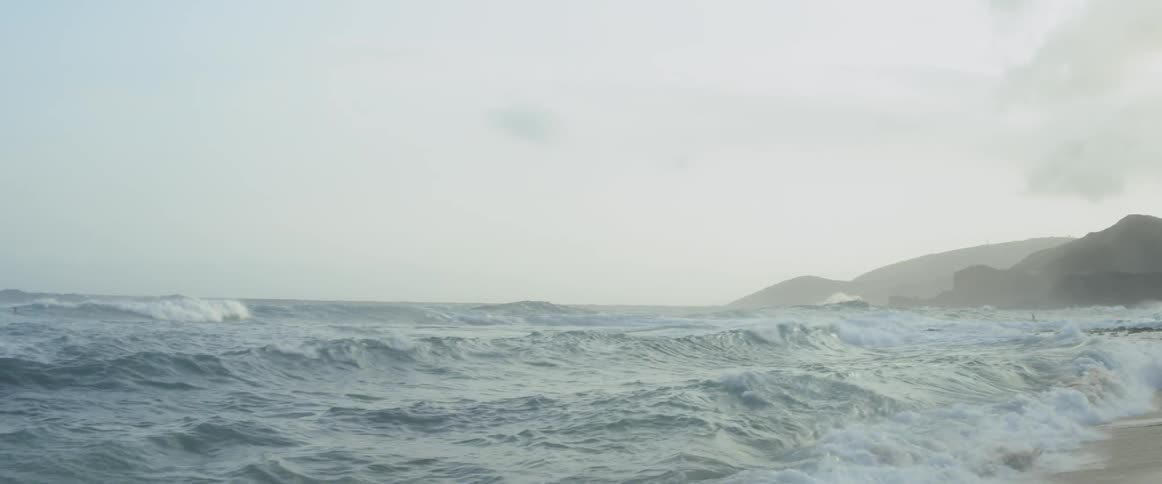 A man is diving into the waves at a beach during the day
