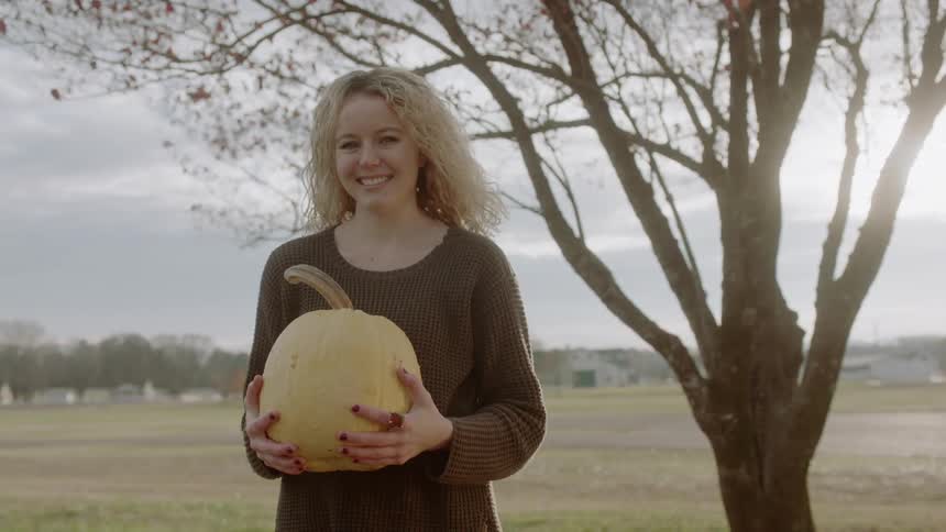 A woman smiles while holding a pumpkin outside